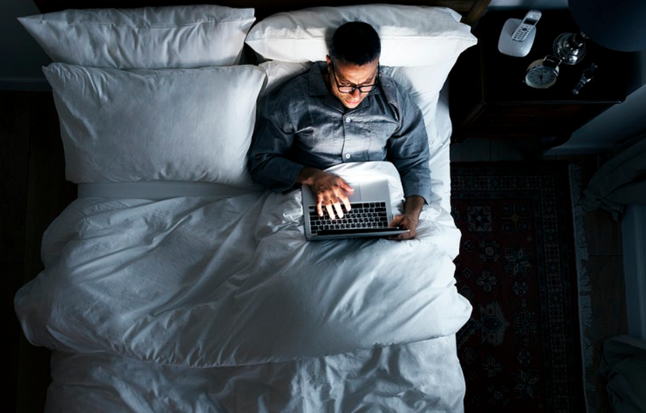 man on pajamas using laptop on bed